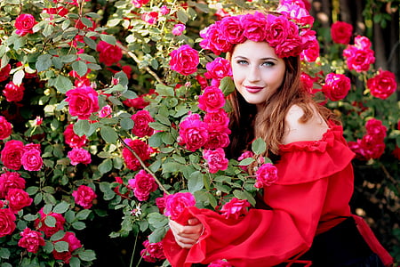 woman wearing red off-shoulder long-sleeved dress while holding red roses during daytime