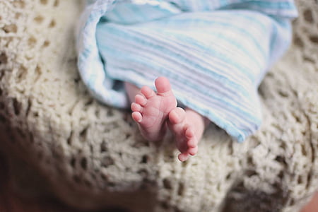 shallow focus photography of infant covered with white and teal blanket