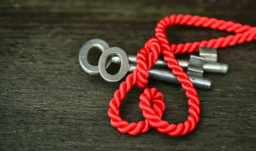two silver keys and red rope on gray wooden surface