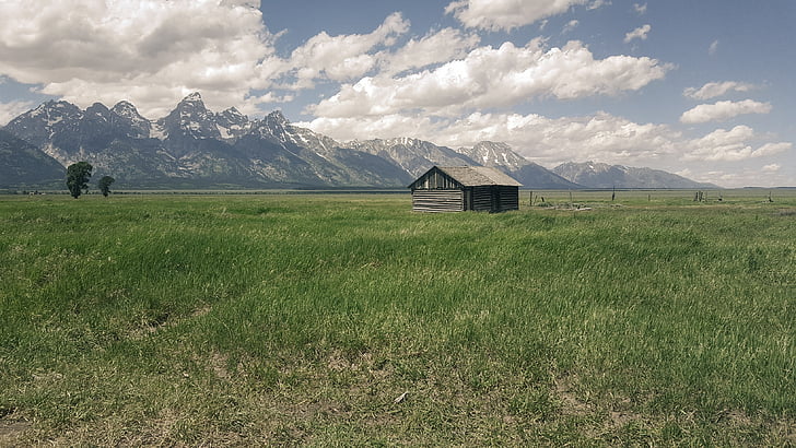 brown wooden shed on middle on grass field in front of mountain