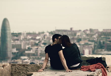 couple sitting on big rock near buildings during daytime