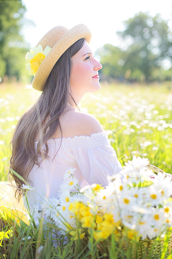 woman wearing white off-shoulder top and brown hat sitting on flower field