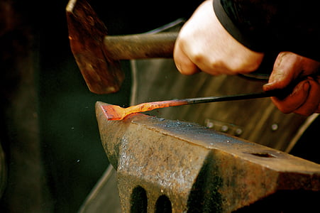 person welding a metal with hammer on anvil