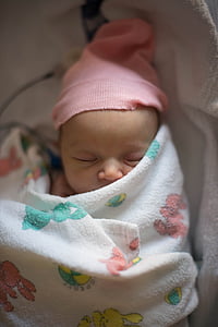 sleeping baby wearing orange knit cap with white and multicolored blanket