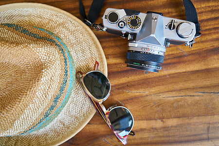 black and gray DSLR camera beside a sunglasses and hat on table