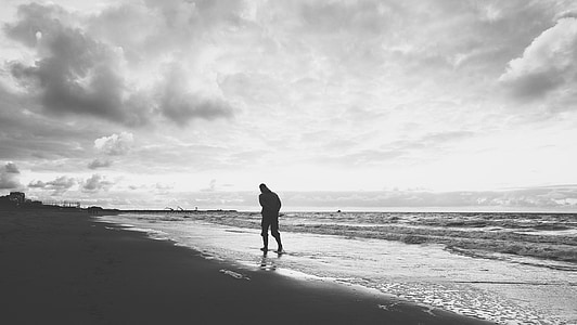 grayscale photo of person walking seashore