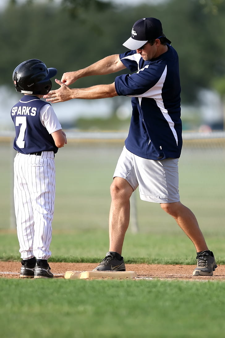 man teaching boy how to swing a bat on base during daytime