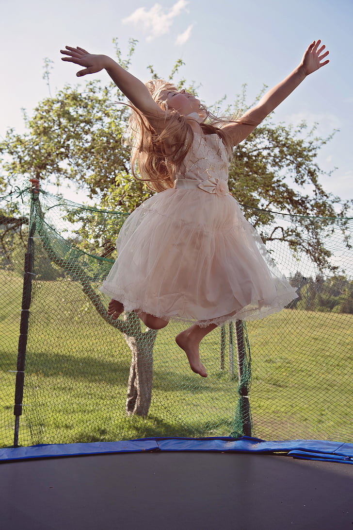 girl in pink dress jumping on trampoline