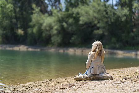 girl wearing white blouse sitting on brown wooden beside body of water during daytime