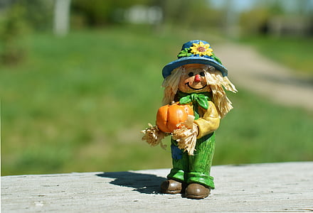 selective focus photography of scarecrow holding pumpkin figurine