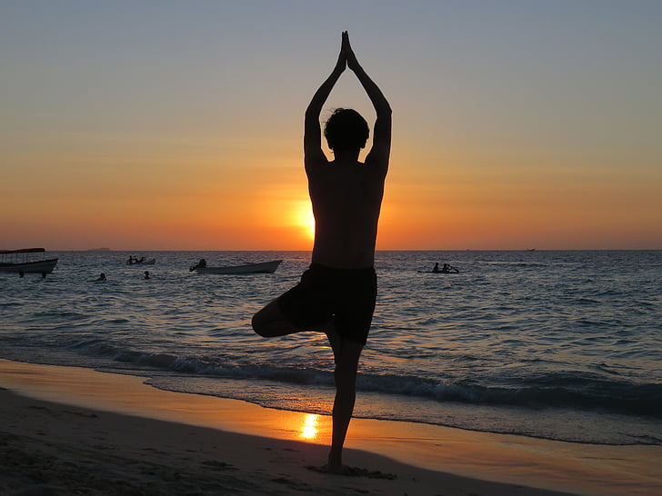 silhouette of person standing on beach doing yoga pose