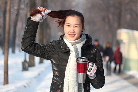 woman holding her hair and grey mug standing on snow covered ground