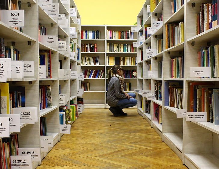woman in gray sweater near book lot on beige cubby shelf