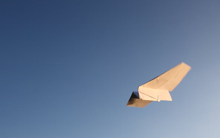 tilt-shift lens photography of white paper plane in flight during daytime