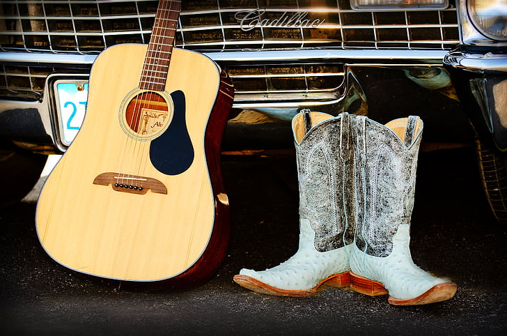 brown dreadnought acoustic guitar beside pair of cowboy boots