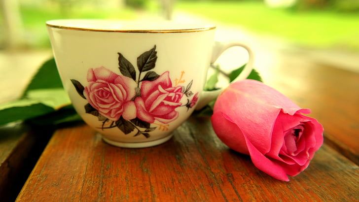 white and pink floral ceramic teacup beside pink rose