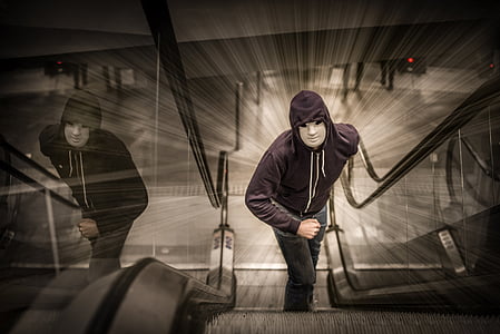 man in white mask and hooded jacket standing on escalator