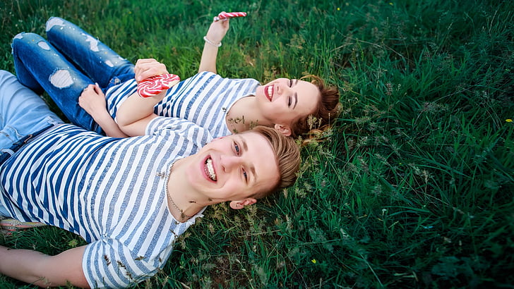 couple wearing gray-and-white striped shirts lying on green grass at daytime