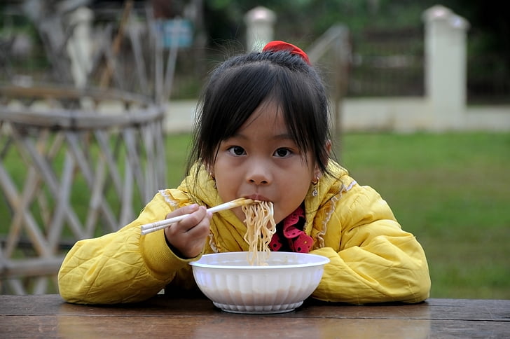 girl in yellow hoodie eatting noodles on table