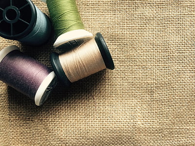 four assorted-color threads with spools over beige canvas textile