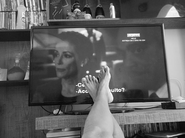 grayscale photo of person's feet in front of flat screen TV
