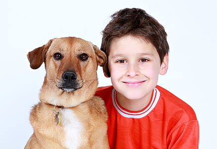 smiling boy wearing red crew-neck shirt beside brown adult Carolina dog