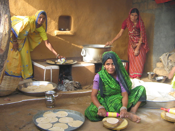 three women baking pancake near house
