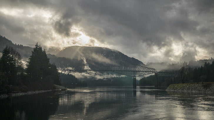 grey metal bridge near black mountain under cloudy sky