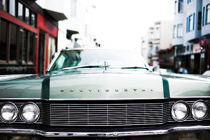 green Lincoln Continental on road near buildings during daytime