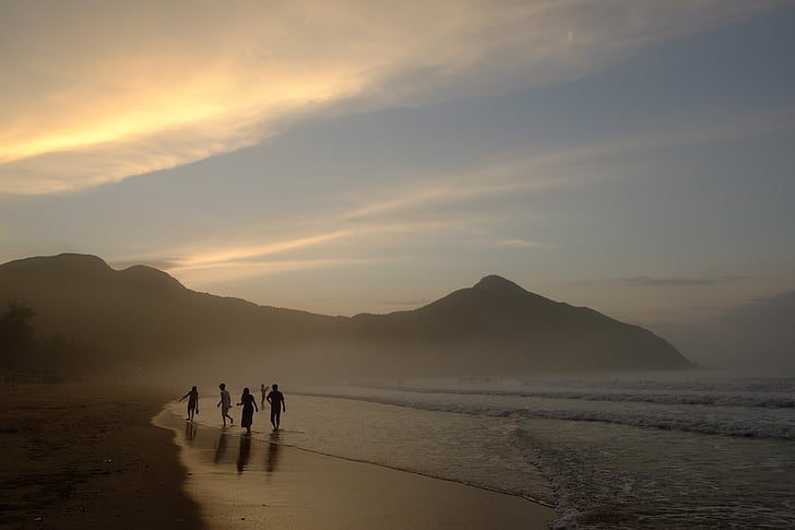 group of people walking on seashore near mountain range under golden hour