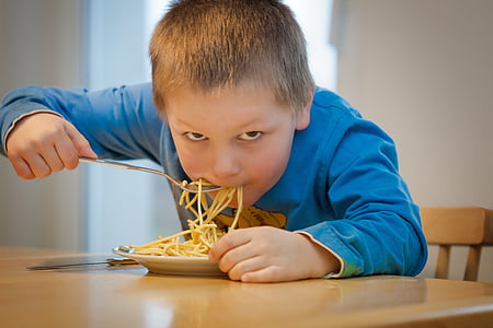 boy in blue sweatshirt eating pasta on brown wooden table during daytime