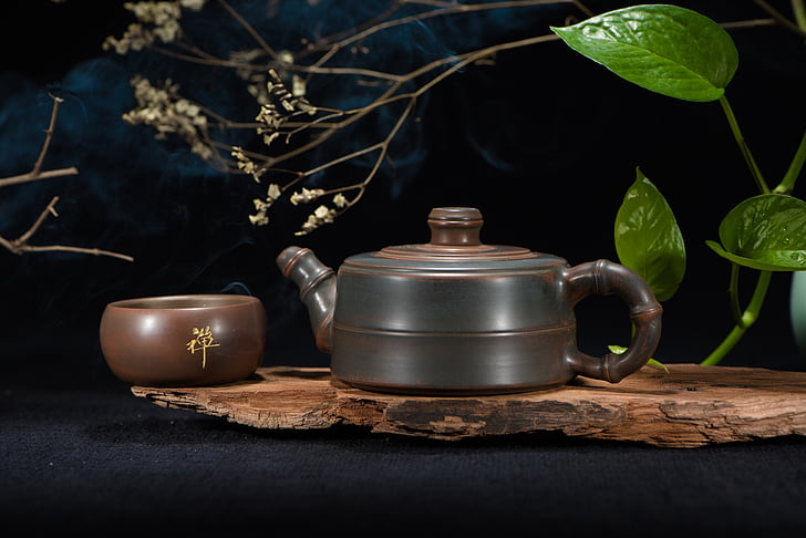 brown and black terracotta kettle on brown wooden slab bear green Ivy plant