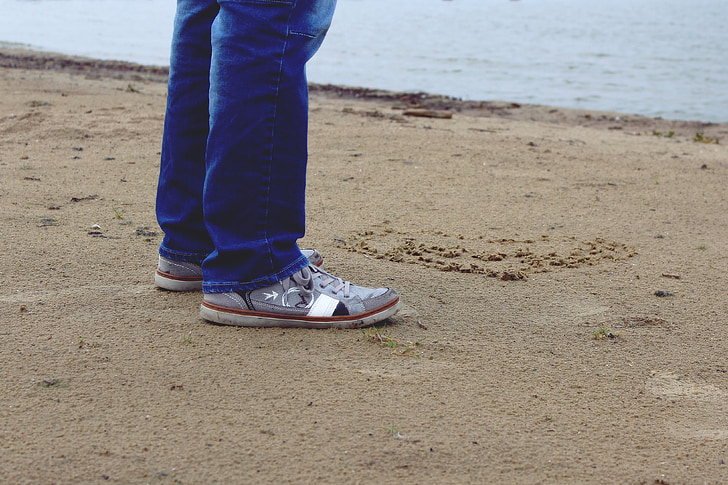 person in jeans and grey sneakers standing on beach sand
