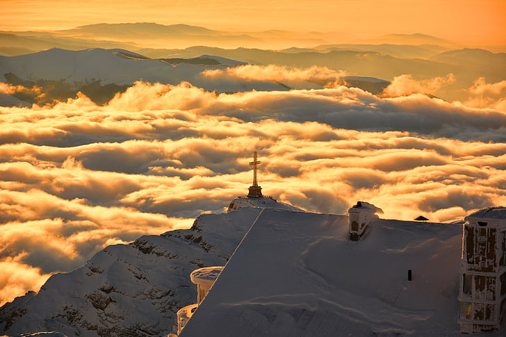 cross on top of snowy mountain surrounded by clouds