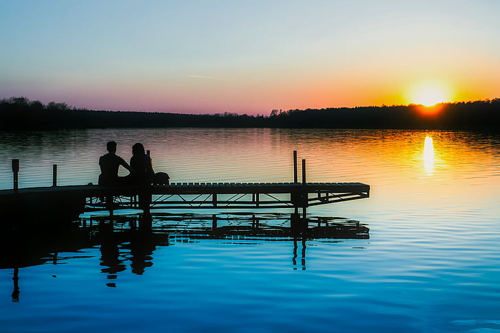 silhouette of two people sitting on docks near body of water