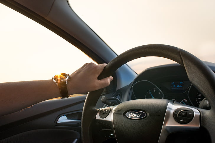 person holding gray Ford car steering wheel during daytime