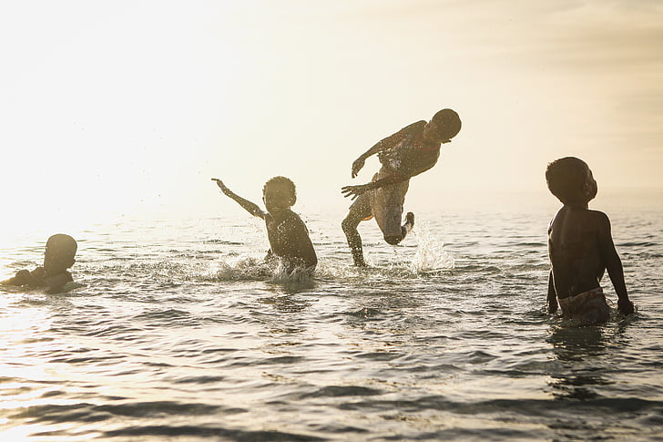 four boys swimming on sea during daytime