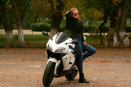woman wearing blue fitted jeans and black zip-up jacket standing beside white Honda sportsbike