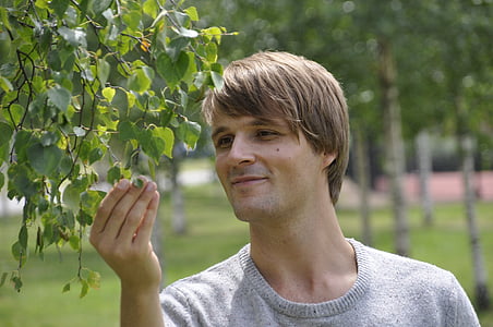 man wearing gray crew-neck top while touching green leaf plants during daytime