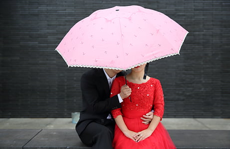 man hugging woman wearing red long-sleeved dress under umbrella