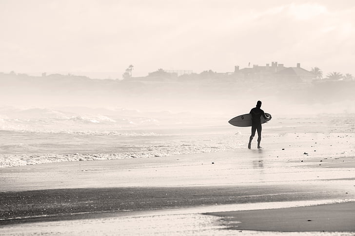 person holding surfboard walking at seashore