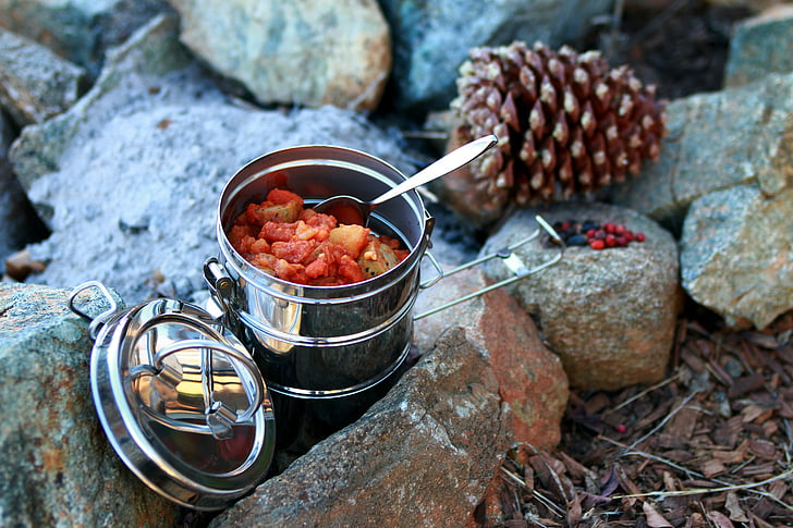 stainless steel tiffin box on rocks near brown pine cone during daytime