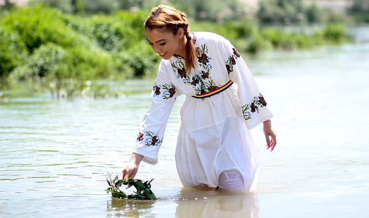 woman wears white and black floral dress stands on water near green grass
