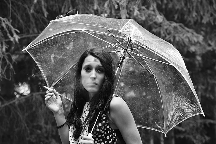 grayscale photo of woman holding umbrella and cigarette stick