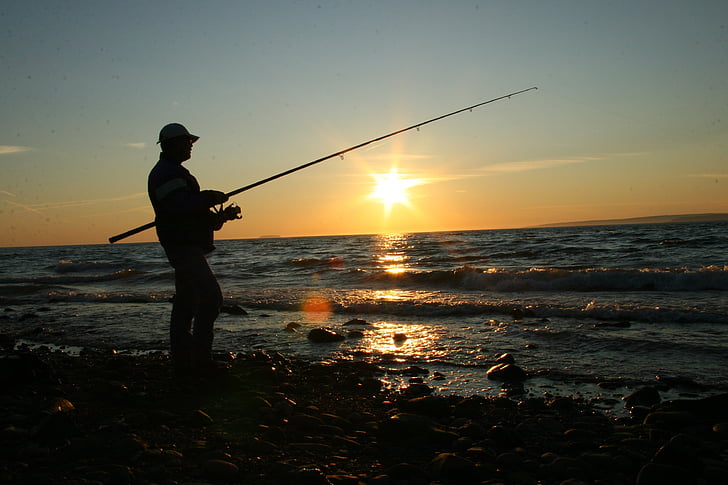 silhouette of person holding fishing rod on beach shore during sunset