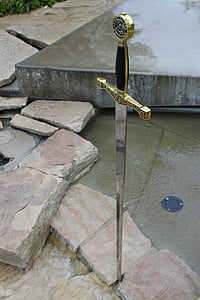 gray stainless steel and brass-colored claymore sword in a stone