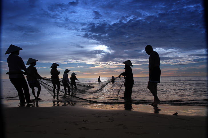 silhouette of people holding fish net on body of water