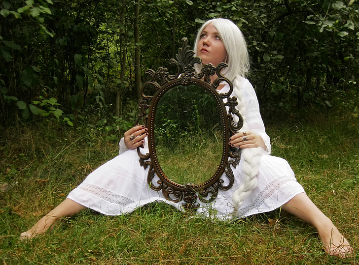 woman wearing white dress holding mirror while sitting on grass at daytime