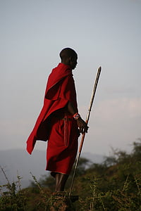 man wearing red top and bottoms holding gray metal spear standing on rock during daytime