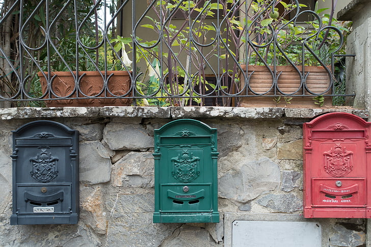 black, green, and red steel mailboxes mounted on gray concrete wall